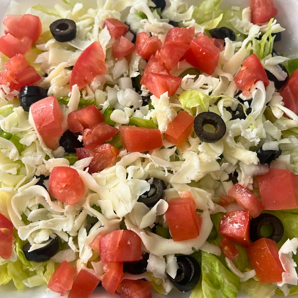 Close-up of a fresh salad with shredded lettuce, diced tomatoes, black olives, and white cheese.
