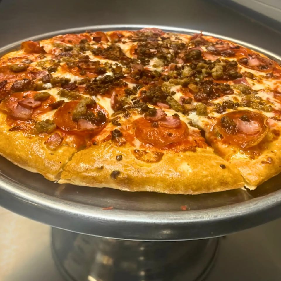 A whole Cicero's Pizza with pepperoni, sausage, and ham on a metal stand.